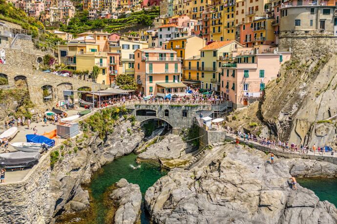 In Manarola, pastel houses rise above a rocky harbor with emerald water and stone walkways.