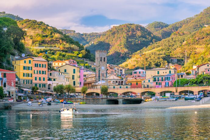 Colorful waterfront houses in Monterosso al Mare lined with a small sandy beach dotted with fishing boats, backed by green hills.