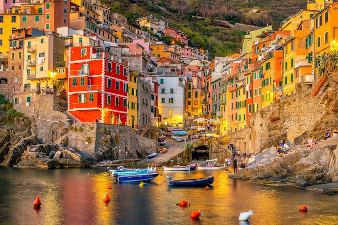 Bright pastel buildings in Riomaggiore stacking dramatically on the cliffs above a tiny harbor filled with boats.