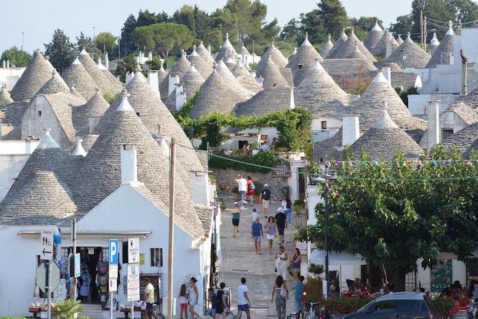 A lively street in Alberobello, Italy, surrounded by iconic Trulli houses with conical stone roofs, with visitors exploring.