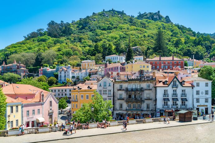 Colorful streets and historic buildings in Sintra beneath the forested hills crowned by the ruins of the Moorish Castle.