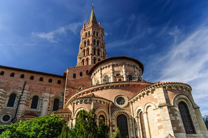 Romanesque church in Toulouse with brick architecture, rounded apse, and bell tower under a bright blue sky.