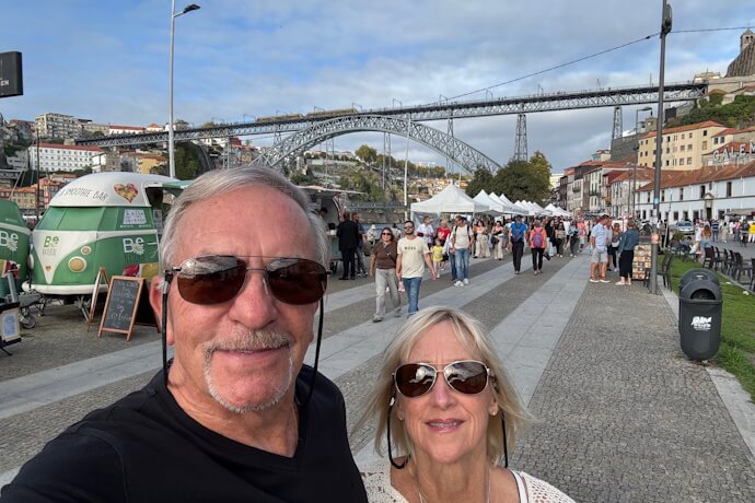 A couple posing along Porto’s riverfront promenade with the Dom Luís I Bridge and market stalls in the background.