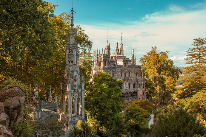 The mysterious Quinta da Regaleira in Sintra, featuring ornate stone architecture with towers and intricate details, surrounded by lush green trees.