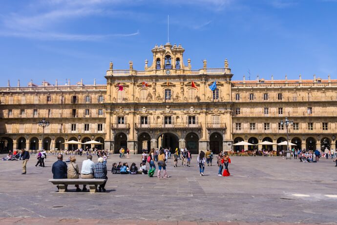 Wide square in Salamanca, Spain, surrounded by golden sandstone arcades, with people sitting, walking, and enjoying the lively atmosphere.