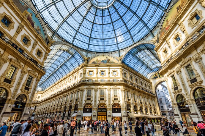 The elegant glass-domed interior of Galleria Vittorio Emanuele II in Milan, bustling with visitors under the ornate architecture and luxury storefronts.