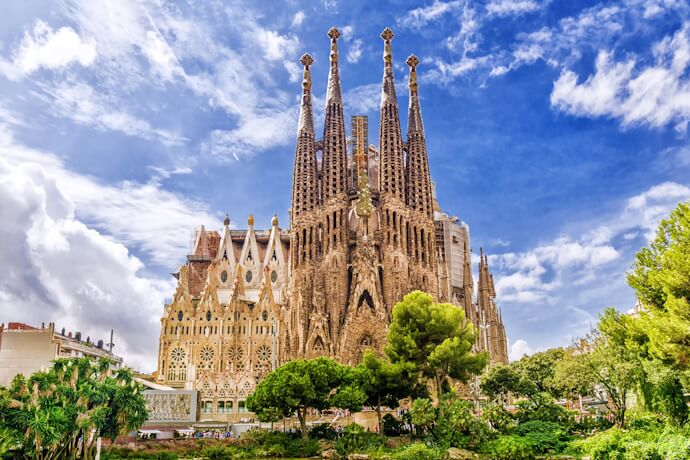 Colorful mosaic benches and flowing shapes in Park Güell, overlooking Barcelona at sunset with Gaudí’s distinctive architecture in the foreground.