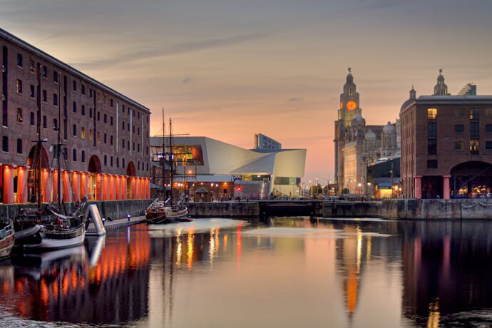 Evening view of Liverpool’s Royal Albert Dock with boats and the city skyline glowing under a colorful sunset.