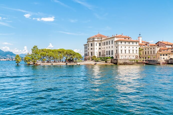 Isola Bella on Lake Maggiore, featuring the Baroque-style Borromeo Palace surrounded by blue waters and lush gardens under a sunny sky.