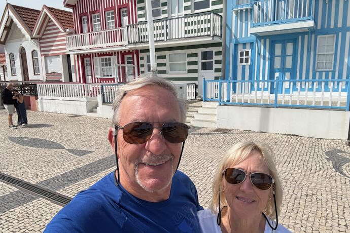 Happy couple posing in front of Costa Nova’s colorful striped houses under bright sunshine.