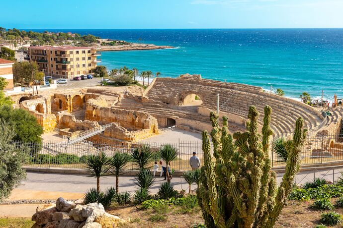 Ancient Roman amphitheater in Tarragona overlooking the Mediterranean Sea, with stone ruins, coastal views, and clear blue water.