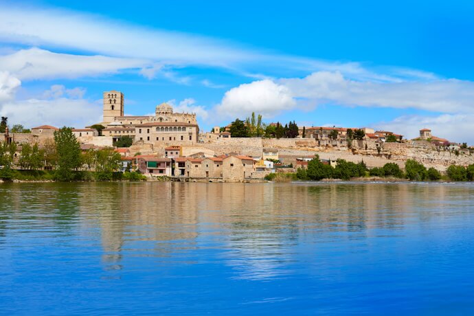 Scenic view of Zamora, Spain, with its Romanesque cathedral and stone buildings reflecting on the calm waters of the Duero River.