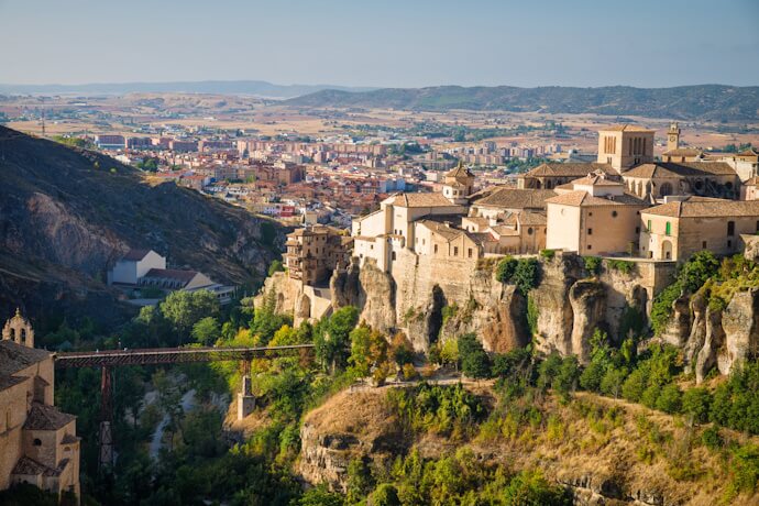 Panoramic view of Cuenca’s cliffside old town, stone buildings perched above a deep gorge with a bridge spanning the valley.