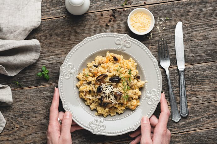 A rustic table setting with a plate of creamy mushroom risotto topped with herbs and grated cheese.