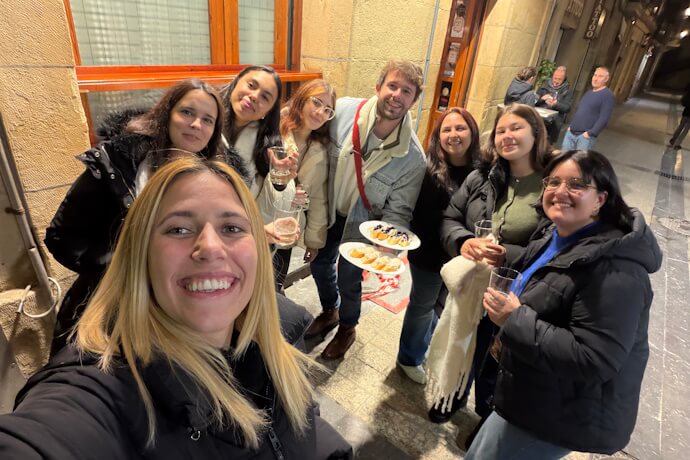 TourTailors Team enjoying pintxos and drinks in Bilbao during an evening food experience, smiling together in a lively old town street.