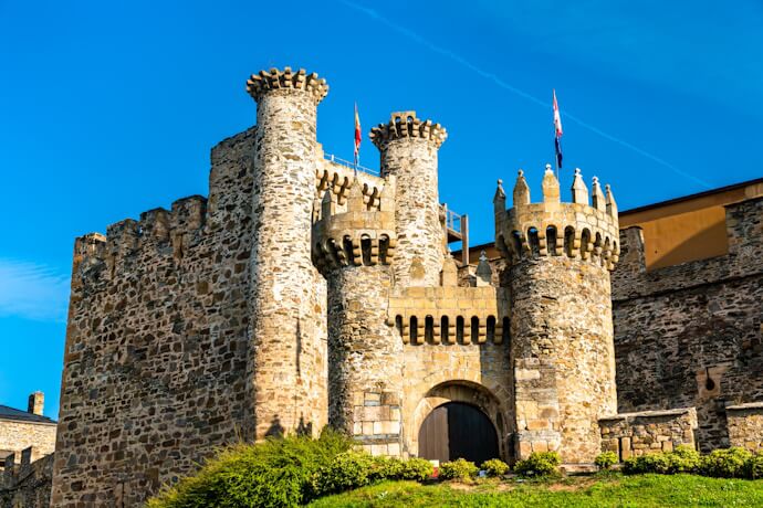 Historic Templar castle in Ponferrada, Spain, with round defensive towers and stone walls under a clear blue sky.