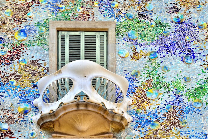 Close-up of a Gaudí-style mosaic façade with a sculpted white balcony and shuttered window at Casa Batlló.