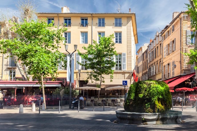 Sunny square in Aix-en-Provence, France, with tree-shaded cafés, historic buildings, and a fountain.