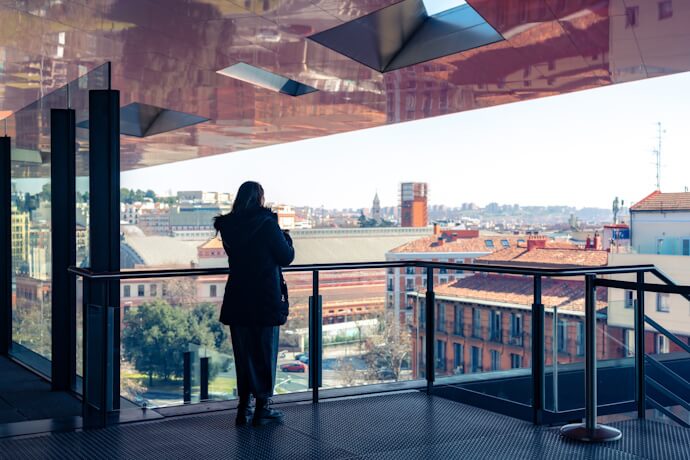 Person looking out over Madrid from a glass terrace at the Reina Sofía Museum, with city rooftops and clear skies in the background.