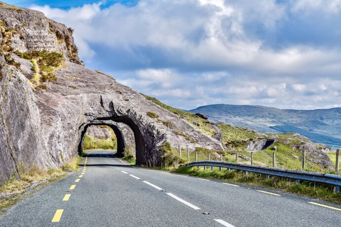 A winding scenic drive through rugged mountains, featuring natural rock tunnels carved into the landscape.