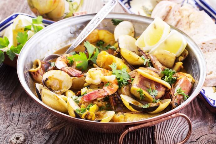 Traditional Portuguese seafood cataplana, served in a copper pan with lemon wedges and rustic bread.