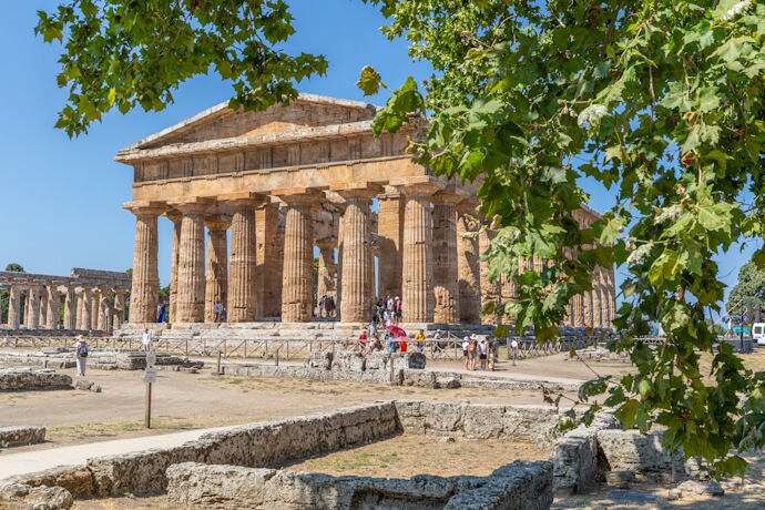 Ancient Greek Temple of Neptune framed by greenery in the archaeological site of Paestum, southern Italy.
