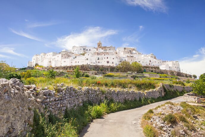 Whitewashed hilltop town of Ostuni with narrow streets, stone walls, and surrounding countryside in Puglia.