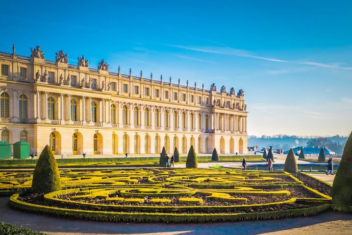 Elegant gardens and the grand façade of the Palace of Versailles under clear blue skies.