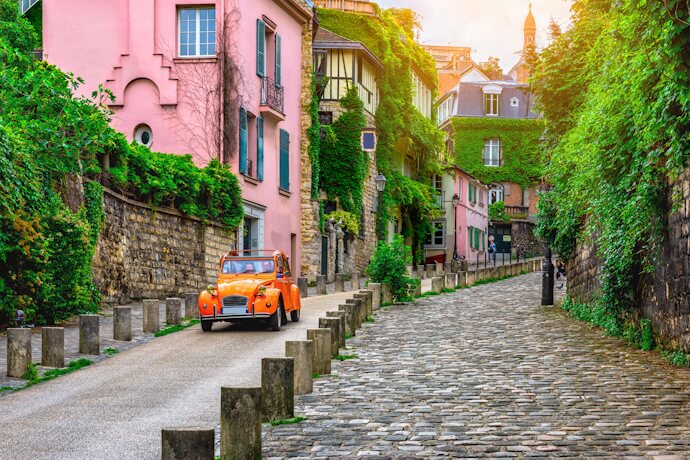 Picturesque cobblestone street in a historic French village with ivy-covered houses and a vintage car.