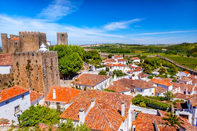 Scenic view of Óbidos showcasing a medieval stone castle and defensive walls surrounded by whitewashed houses with red-tiled roofs