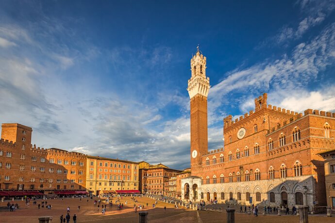 Wide view of Piazza del Campo in Siena with the brick square and the Torre del Mangia tower rising above.