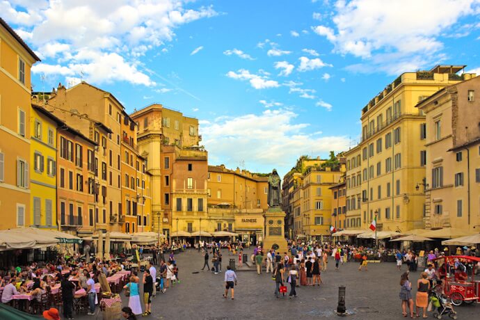 Campo de’ Fiori in Rome, with open-air restaurants and people gathering around the central statue.
