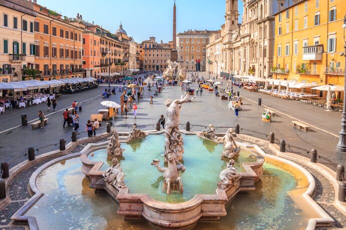 Piazza Navona in Rome with its central fountain, colorful buildings, and visitors strolling the wide square.