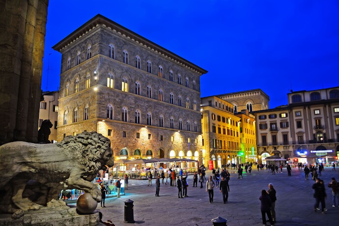 Evening scene in Florence’s Piazza della Signoria, with lit-up buildings and people walking.