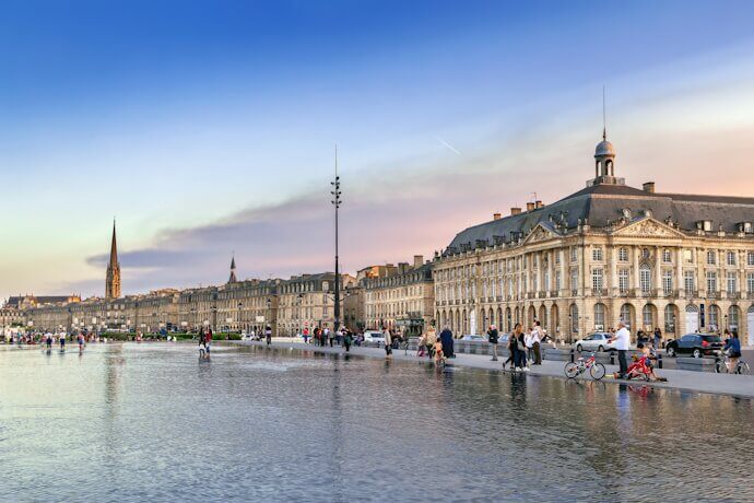 Place de la Bourse in Bordeaux with its water mirror reflecting historic buildings at sunset.