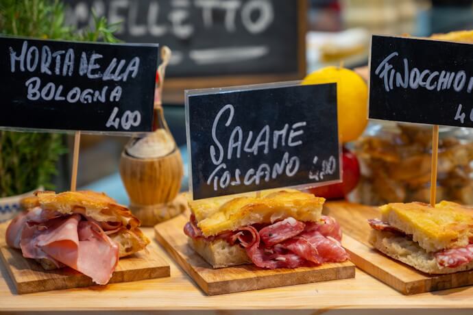 A market-style display showcasing traditional sandwiches piled with cured meats.