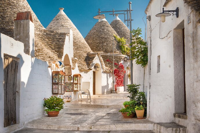 A quiet lane in Alberobello, featuring whitewashed trulli houses with cone-shaped roofs and small flower-filled corners.