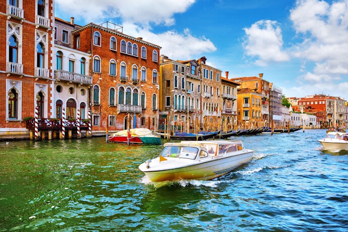 A sunlit canal in Venice running between historic palaces as a small motorboat glides across the water.
