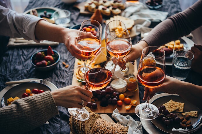 Friends toasting with rosé wine around a table filled with Italian antipasti, bread, cheese, and fresh fruit