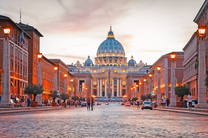 Sunset view of St. Peter’s Basilica in Vatican City, with glowing streetlights and people