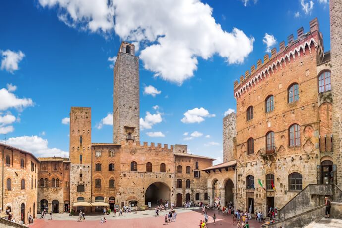 Medieval towers and historic buildings in Piazza della Cisterna, San Gimignano, Tuscany, with visitors walking across the square