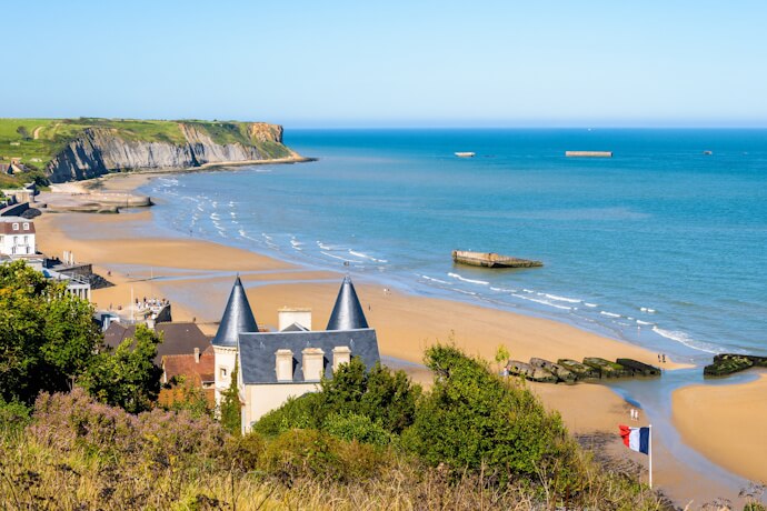 Golden sandy beach and dramatic coastline in Normandy with remnants of the D-Day landing sites along the shore.