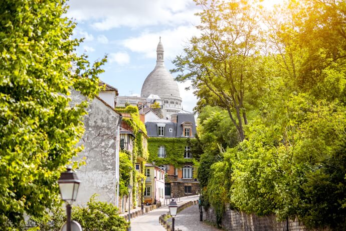 Charming Parisian street in Montmartre framed by greenery with the Sacré-Cœur Basilica rising above.