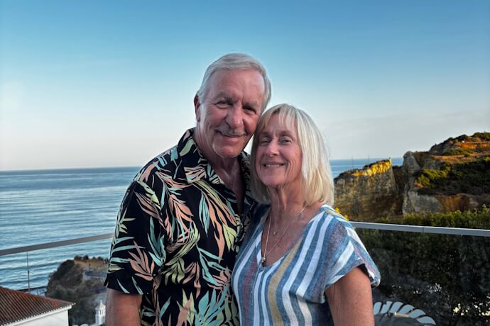 Smiling couple at sunset in Lagos, Algarve, Portugal, with the ocean and golden cliffs in the background.