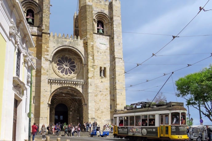  Yellow tram in front of Lisbon Cathedral with tourists at the entrance.