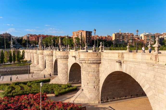Stone arches and landscaped riverside paths along Madrid Río, a modern park area beside the Manzanares River.