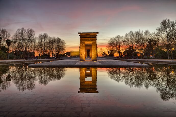 Temple of Debod in Madrid at sunset with reflections across the water and panoramic city views.
