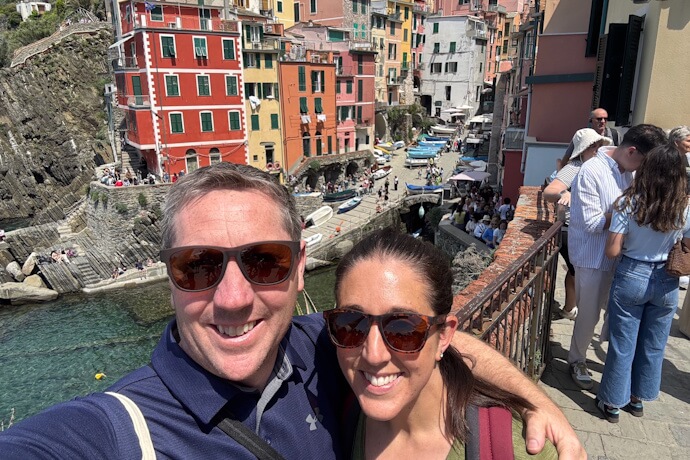 Smiling couple in Riomaggiore taking a selfie with the typical colorful houses of the Cinque Terre in the background
