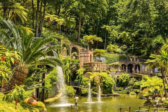 ropical garden with waterfalls, fountains, lush greenery, and historic stone structures