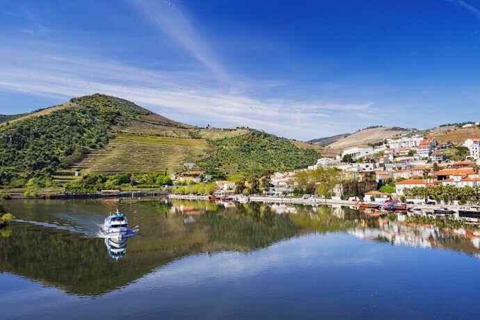 Boat crossing Douro River, green landscape and vineyards